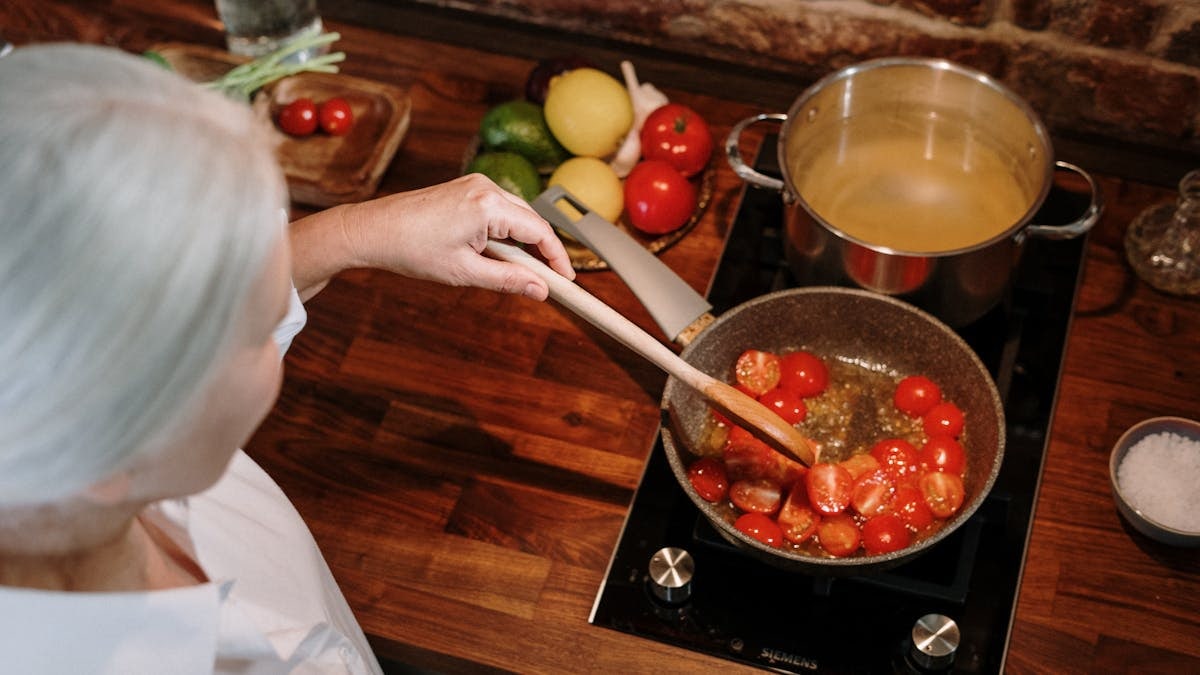 A senior woman prepares a homemade tomato sauce in a warm, cozy kitchen setting.